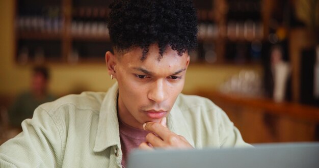 A close-up of a student thoughtfully writing an essay for their college application, with a laptop displaying a college website in the background.